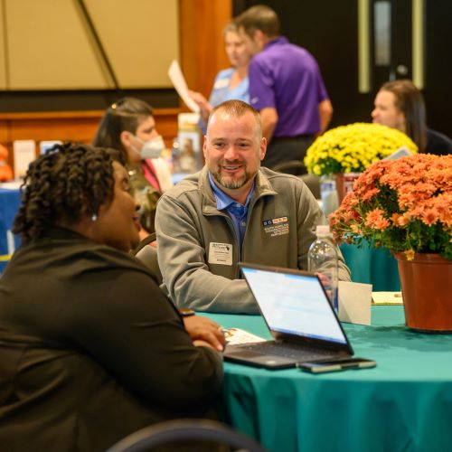 A white man speaks with a Black woman at a table at a previous summit event.