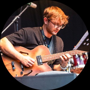 Andrew Tomlinson, a white man with glasses on guitar